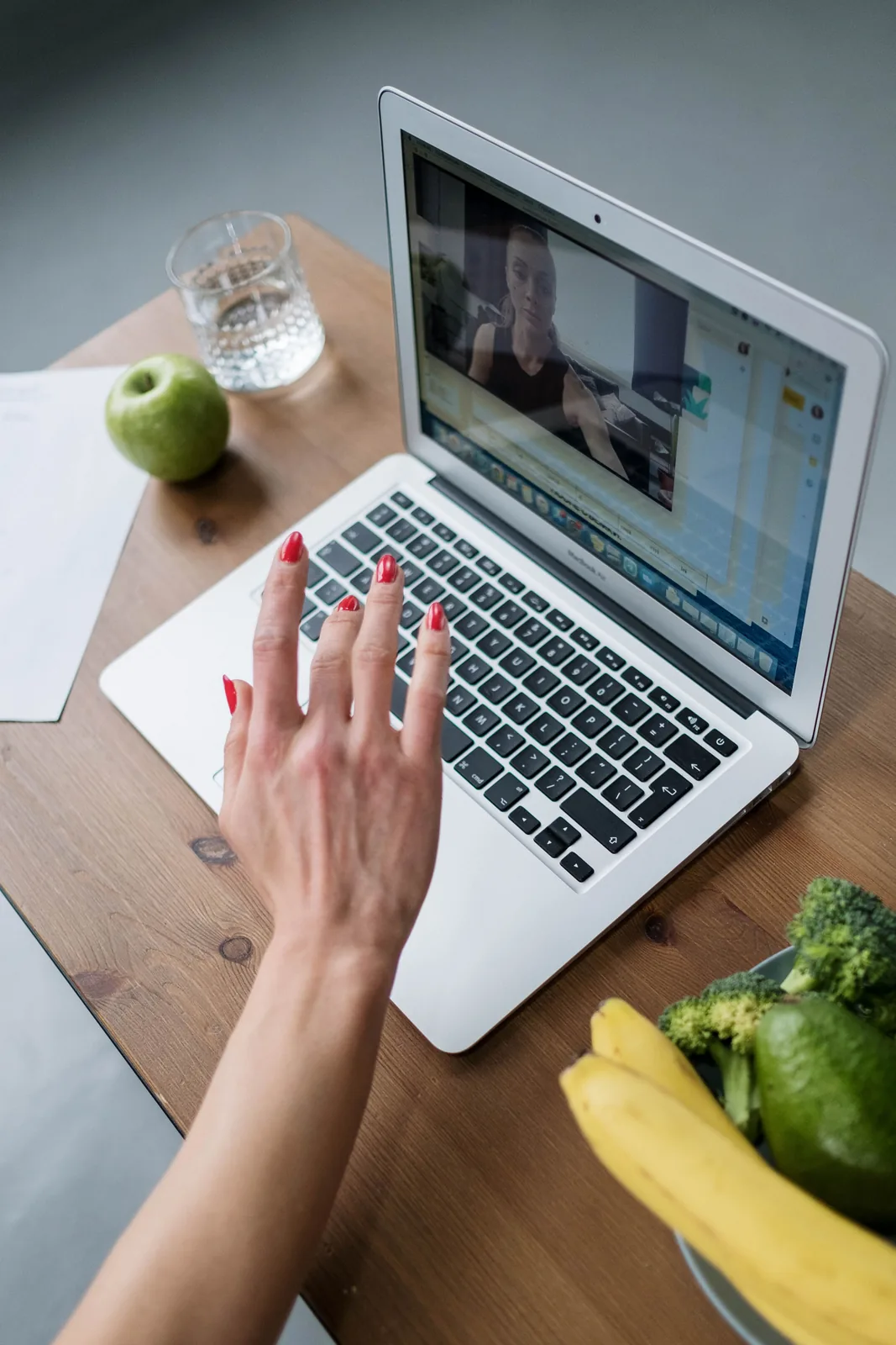 A woman on a video visit at her desk, with fresh fruit and vegetables beside her laptop