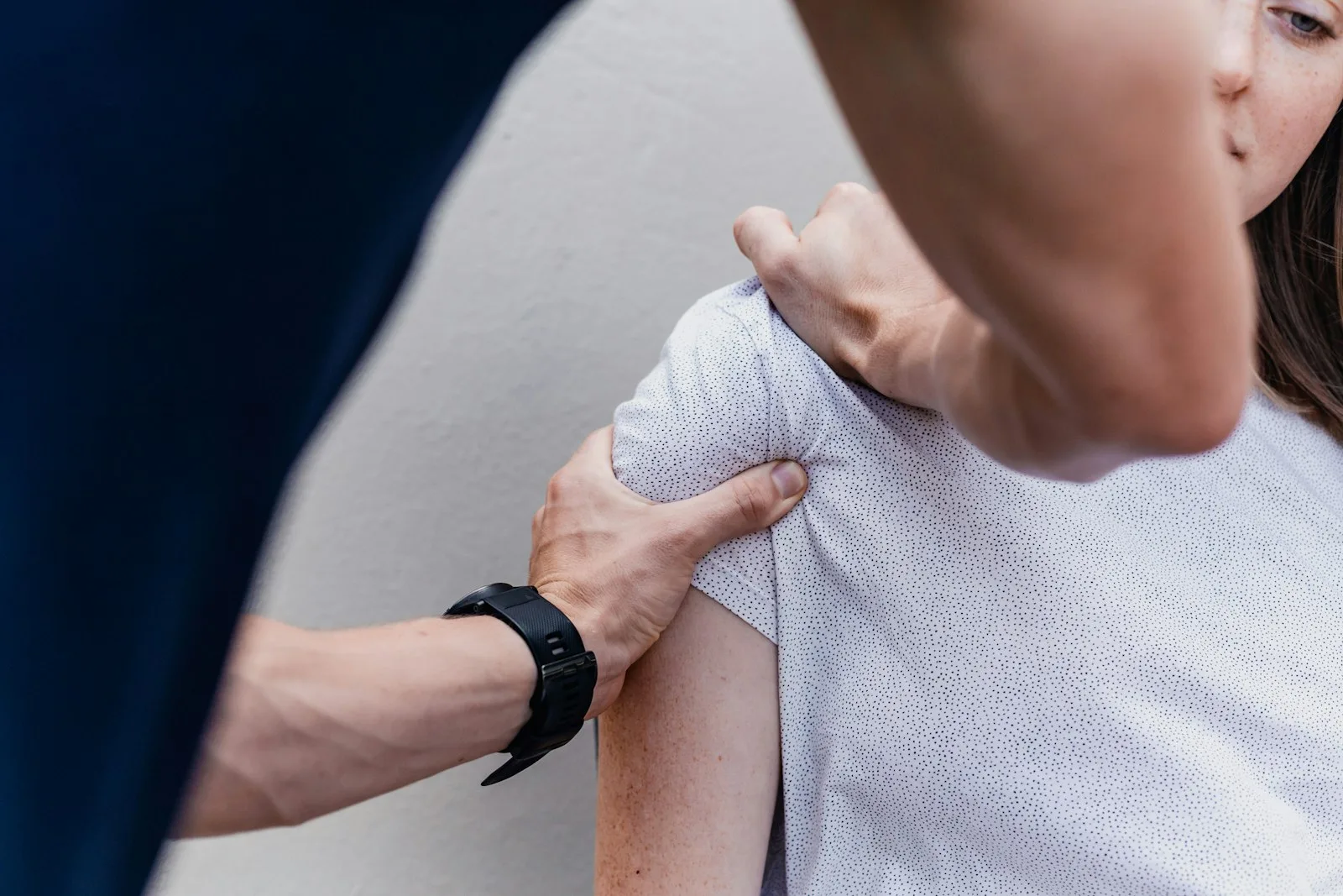 A clinician examining a patient's shoulder with both hands