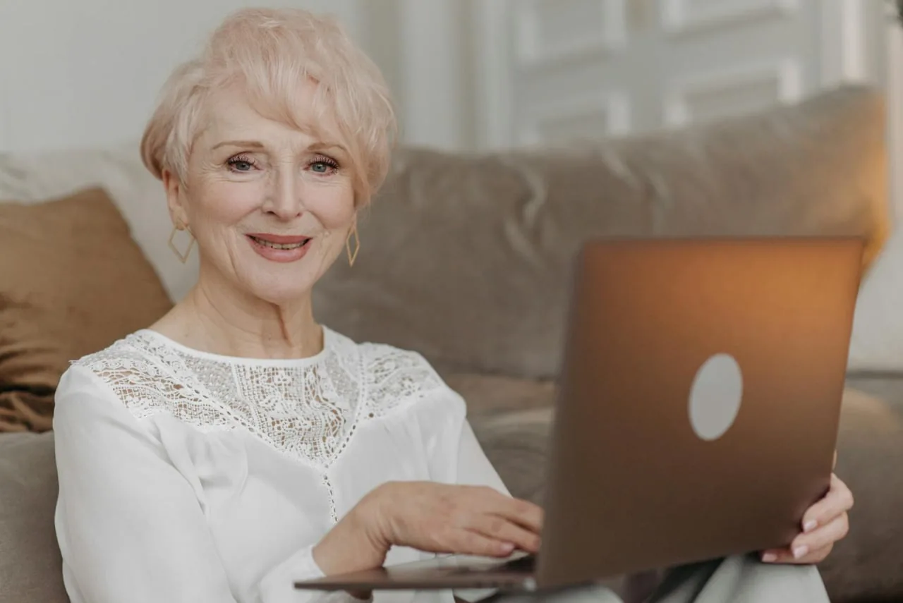 A smiling woman on her couch with a laptop, joining a video visit from home
