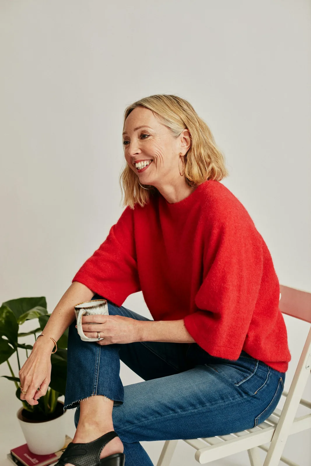 A smiling woman with short blonde hair in a red sweater holding a mug