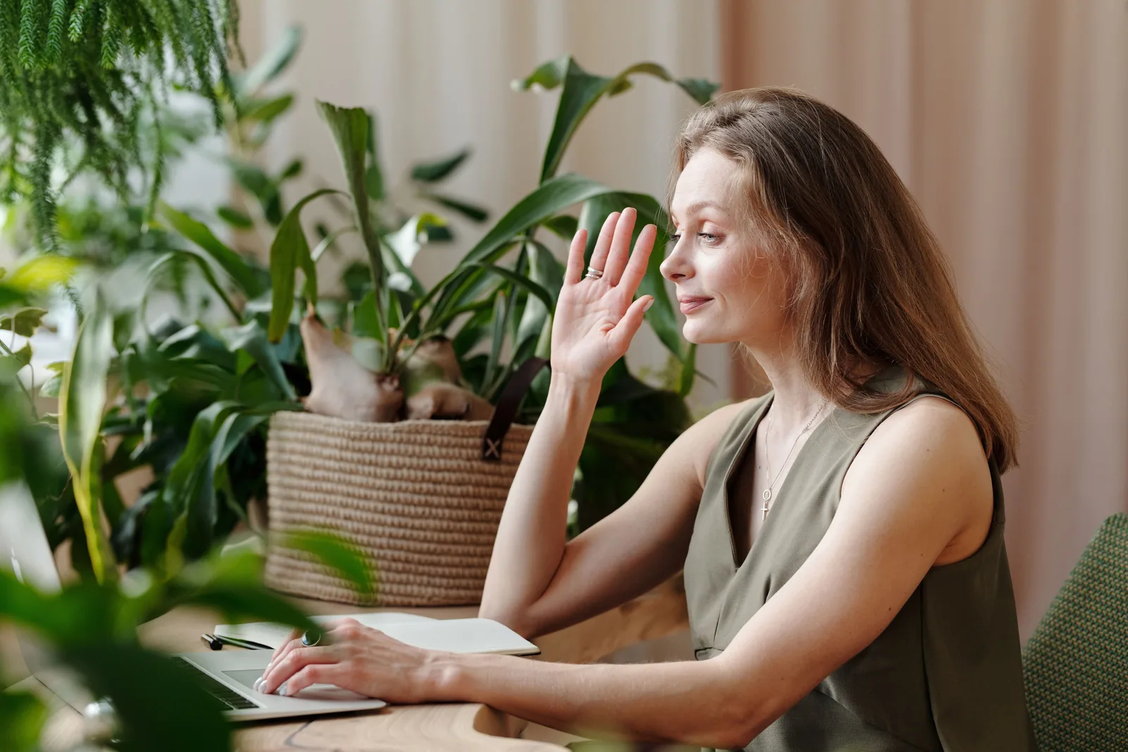 A woman working from home surrounded by plants, smiling warmly during a video call, representative of staying connected with a care team through the menopause transition