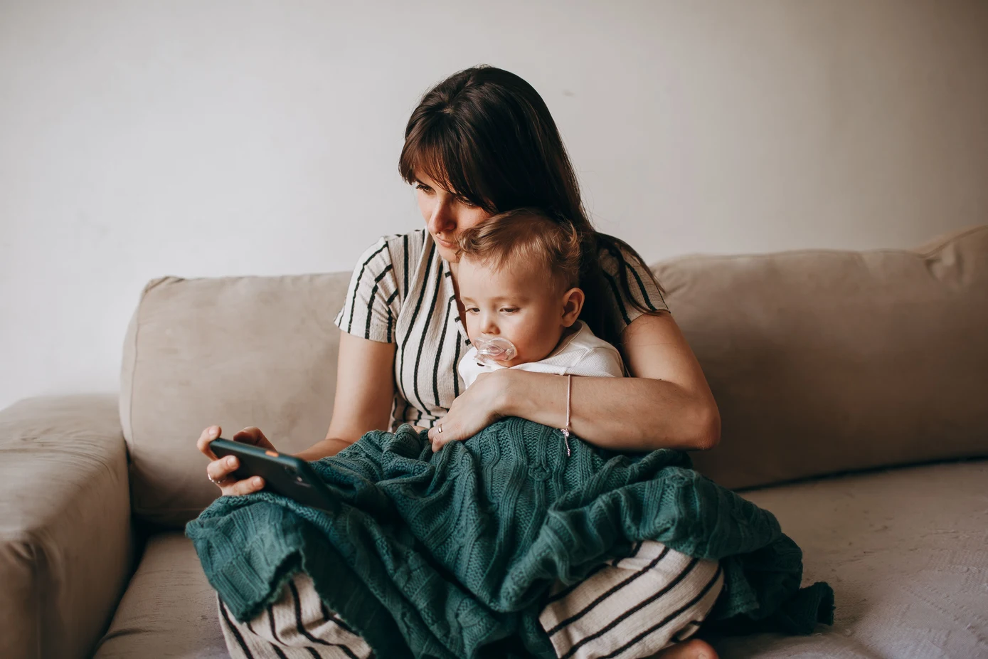A mother holding her baby while looking at her phone to book an appointment