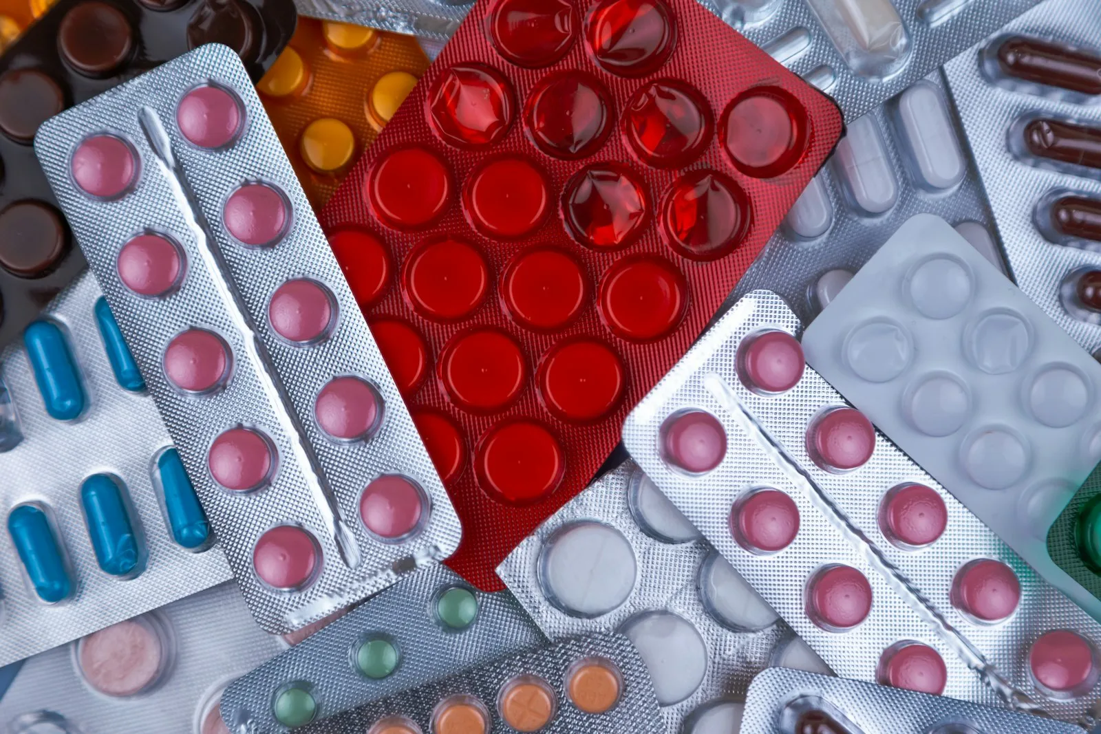 Colorful blister packs of tablets and capsules piled together