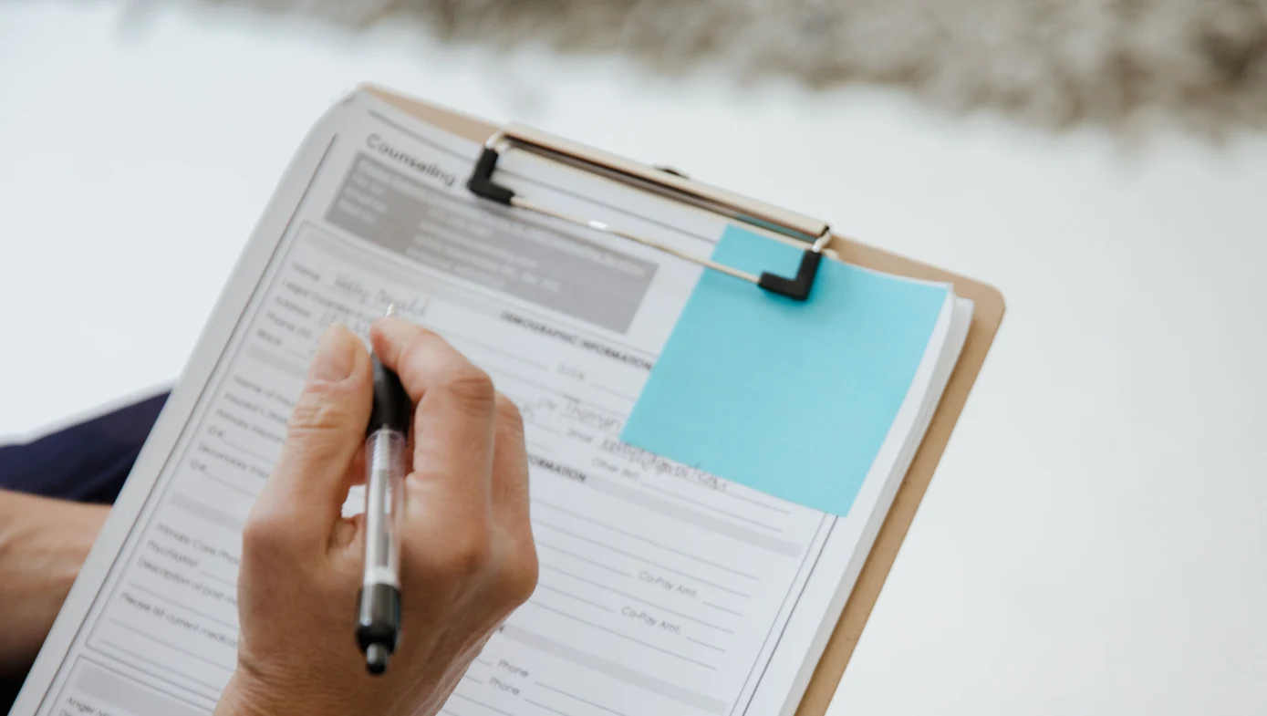 A hand filling out a patient intake form on a clipboard