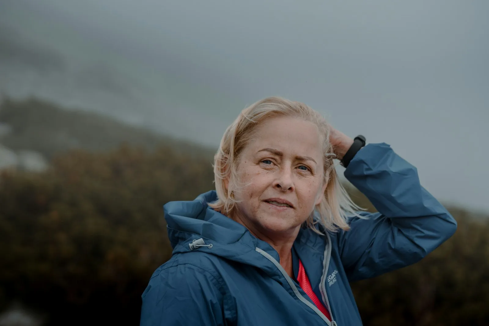 A woman outdoors on a windy day with her hand pushing back her hair, looking stressed