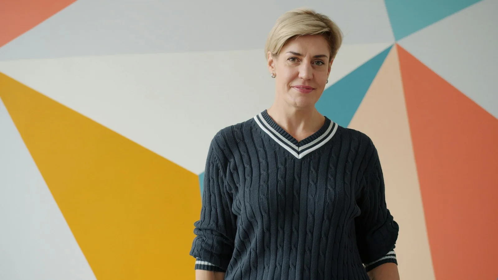 A woman with short blonde hair in a dark sweater standing in front of a colorful wall