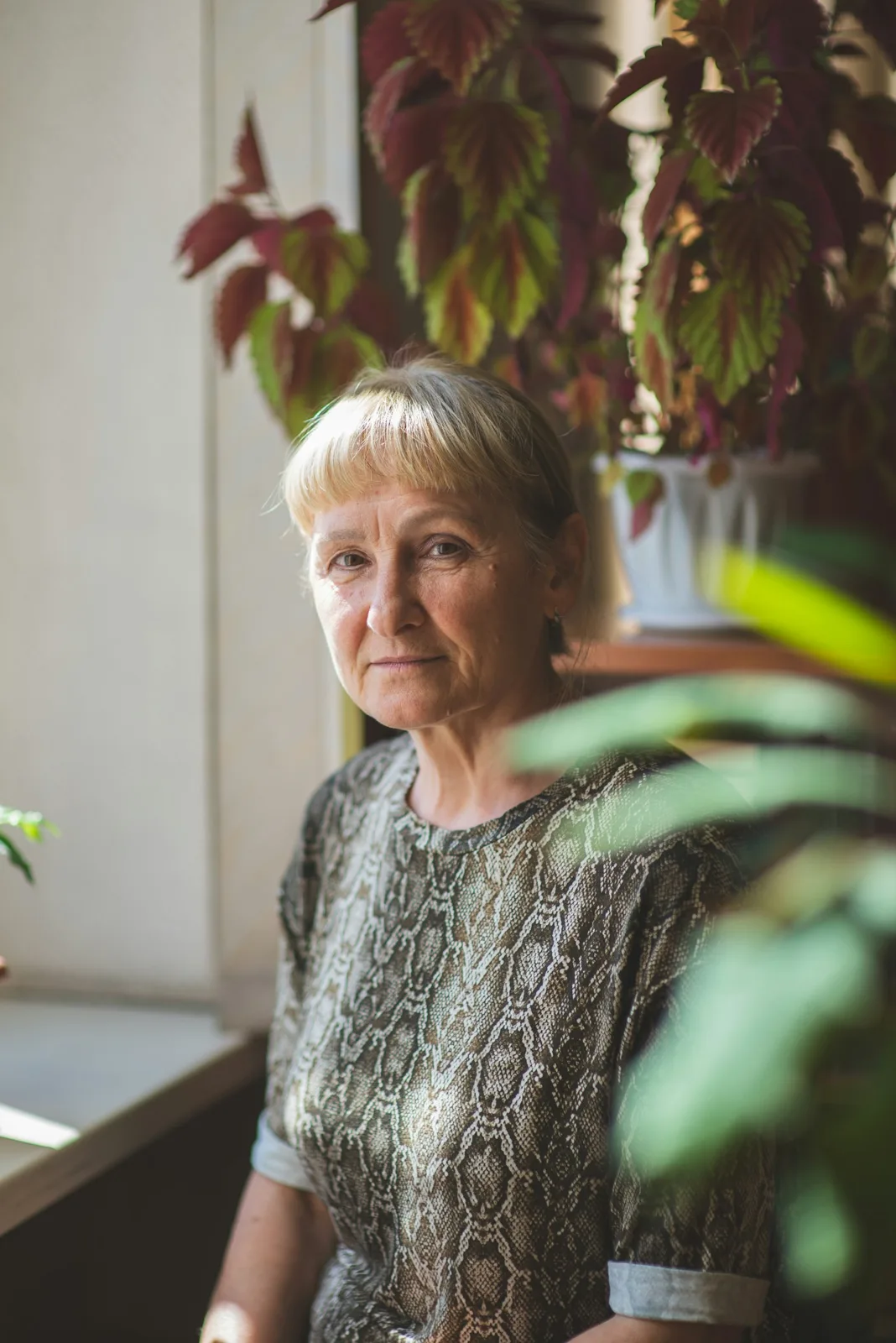 A woman sitting quietly by a sunny window surrounded by plants