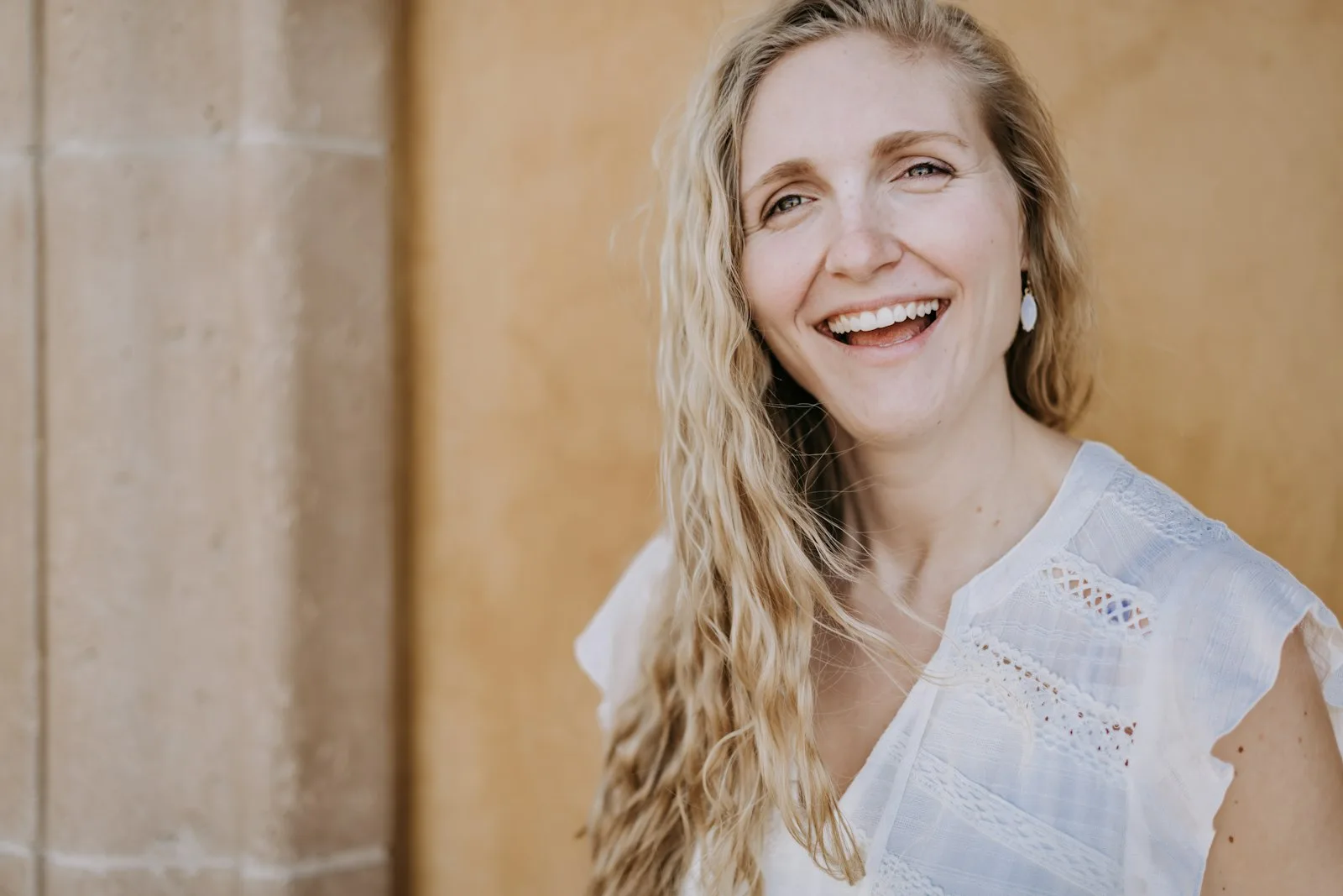 A smiling woman with long wavy blonde hair in a white blouse