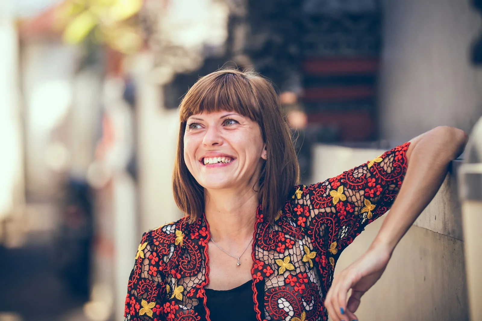 A smiling woman in her forties leaning against a wall outdoors