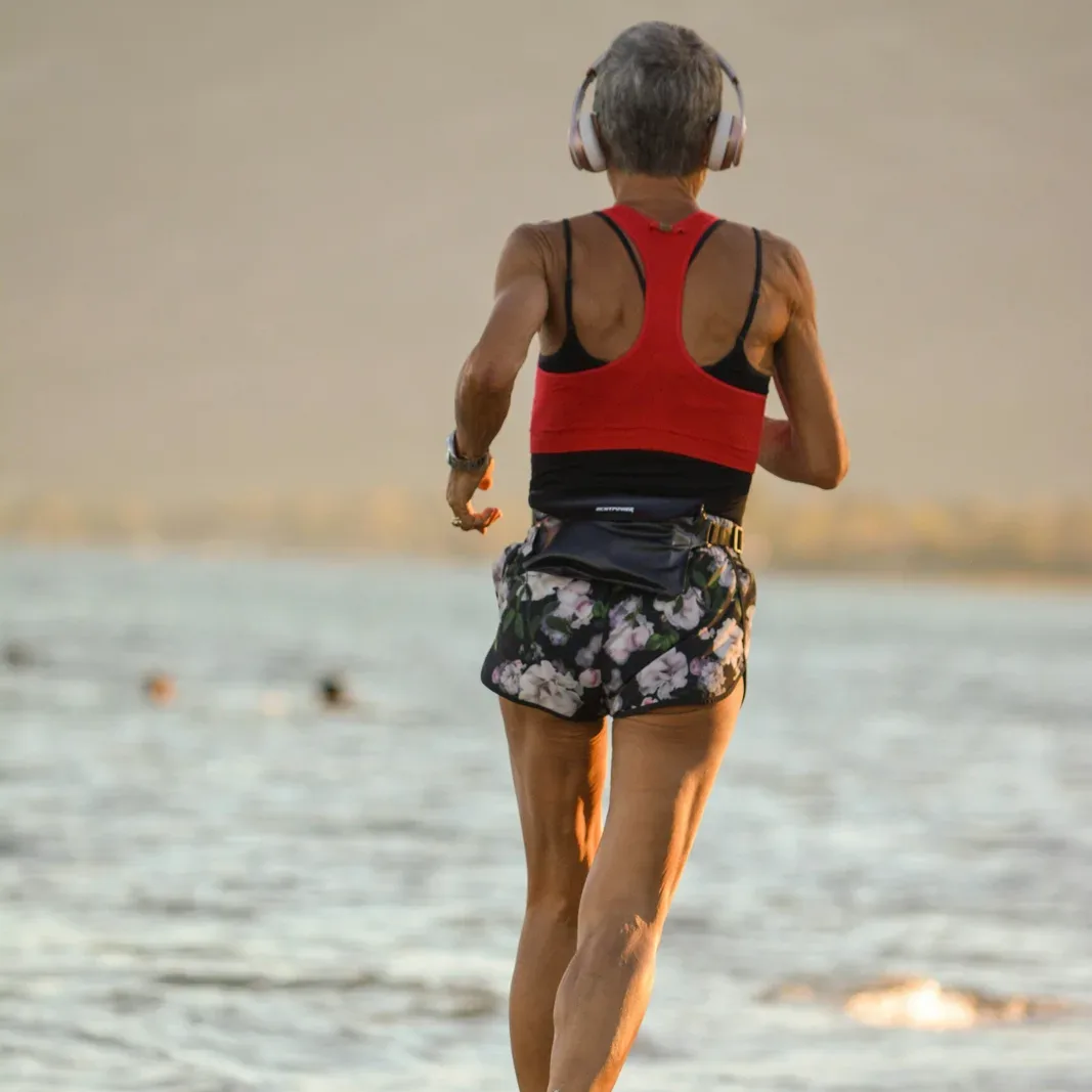 A fit older woman with short gray hair jogging along the water at sunrise